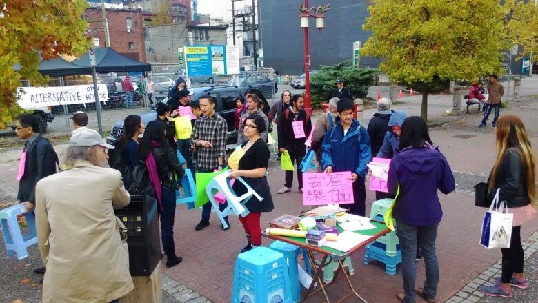 Protesters stand at a site of a proposed condo building. They hold up signs in Mandarin. 