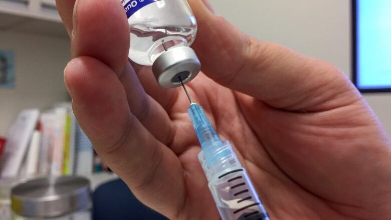 Closeup of a hand holding a bottle of influenza vaccine, with a syringe plunged into it.