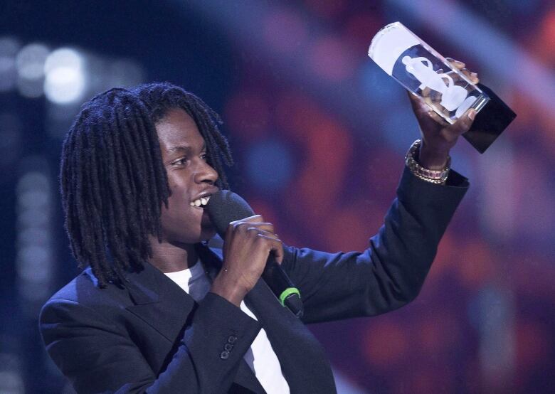 A man holds up an award statue while talking into a microphone.