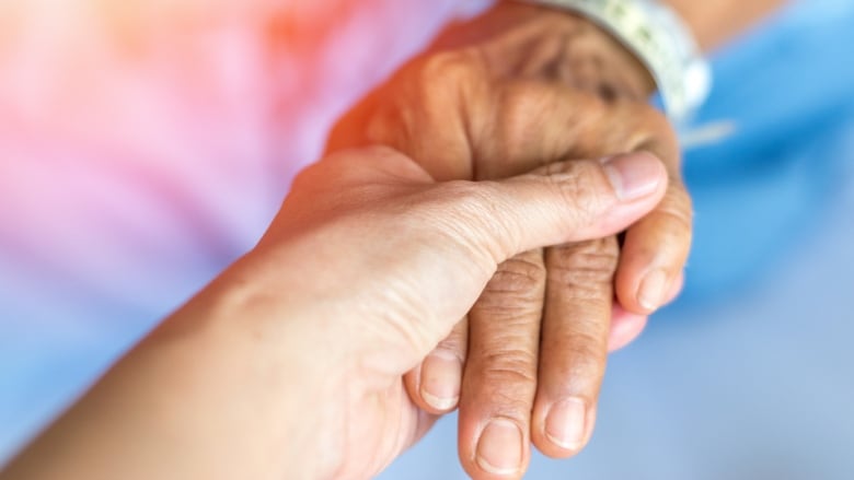 A younger hand clasps the hand of a senior.