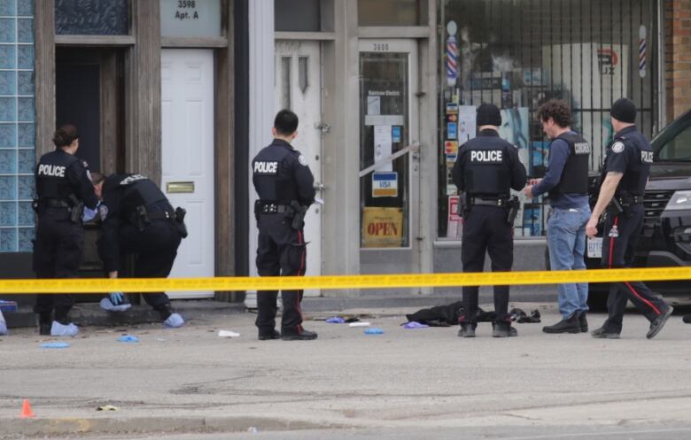 Several police officers standing behind yellow tape at a crime scene.