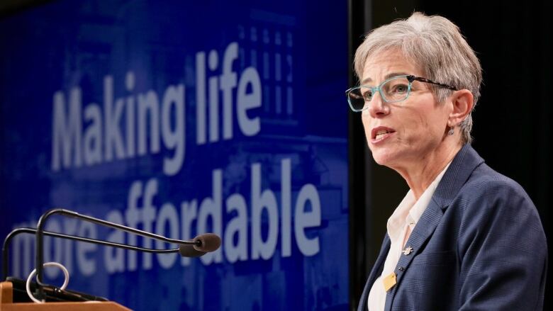 Selina Robinson stands at a podium, with a slide behind her that reads 'Making life more affordable'. She is a white woman with short hair, wearing a navy blue jacket.