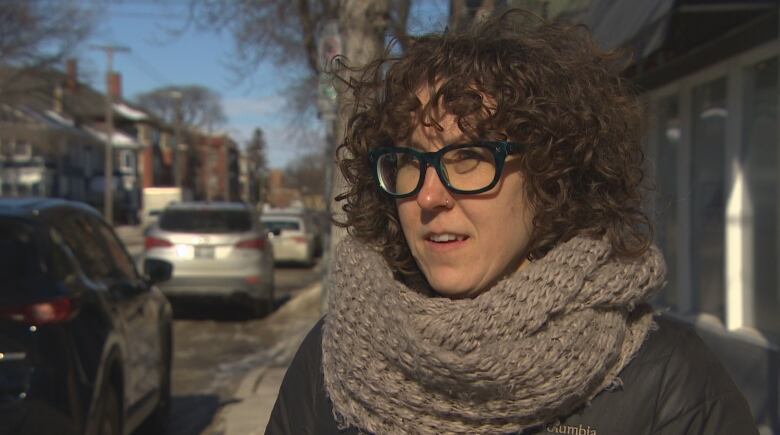 A woman wearing glasses stands outside.