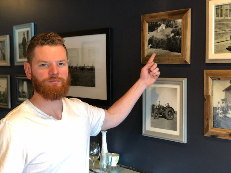 A man points to a framed black-and-white photograph on the wall  one of many of agricultural scenes.