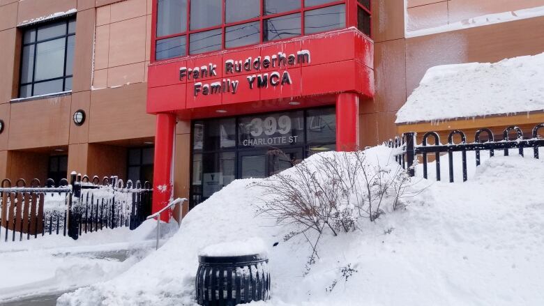 The entrance of a large building on a snowy day. The entrance sign says Frank Rudderham Family YMCA.