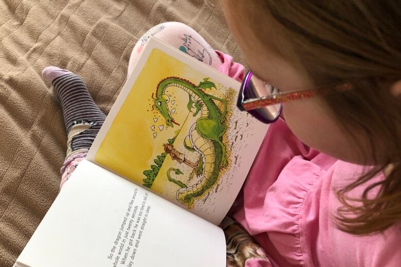 Looking over shoulder of child sitting cross-legged reading a book. An illustration shows a dragon and a young princess wearing a paper bag.