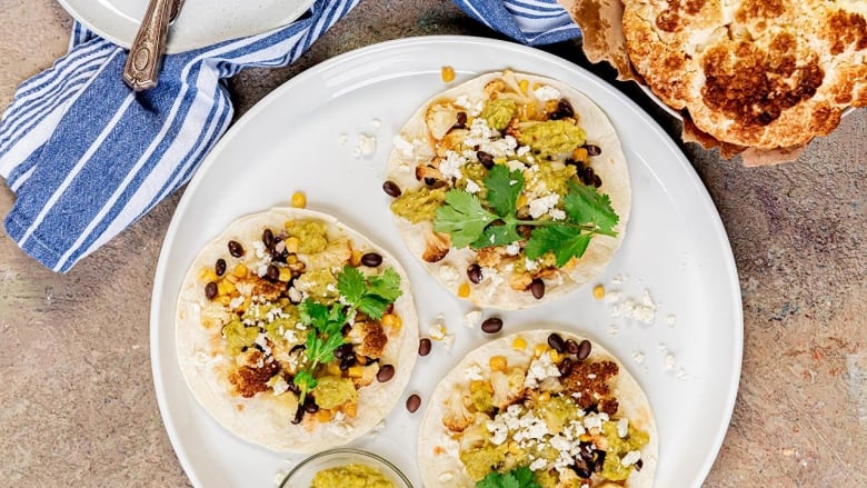 Overhead shot of a white plate with 3 tortillas on it. The tortillas are topped with black beans, corn, Tomatillo Sauce, roasted cauliflower and cilantro. 