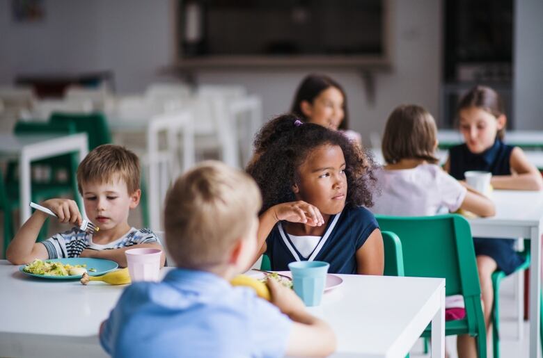 Six elementary school-aged kids sit at two tables eating. 