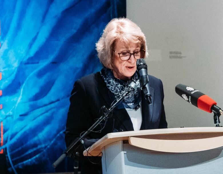 A woman stands at a CBC microphone in an art gallery.