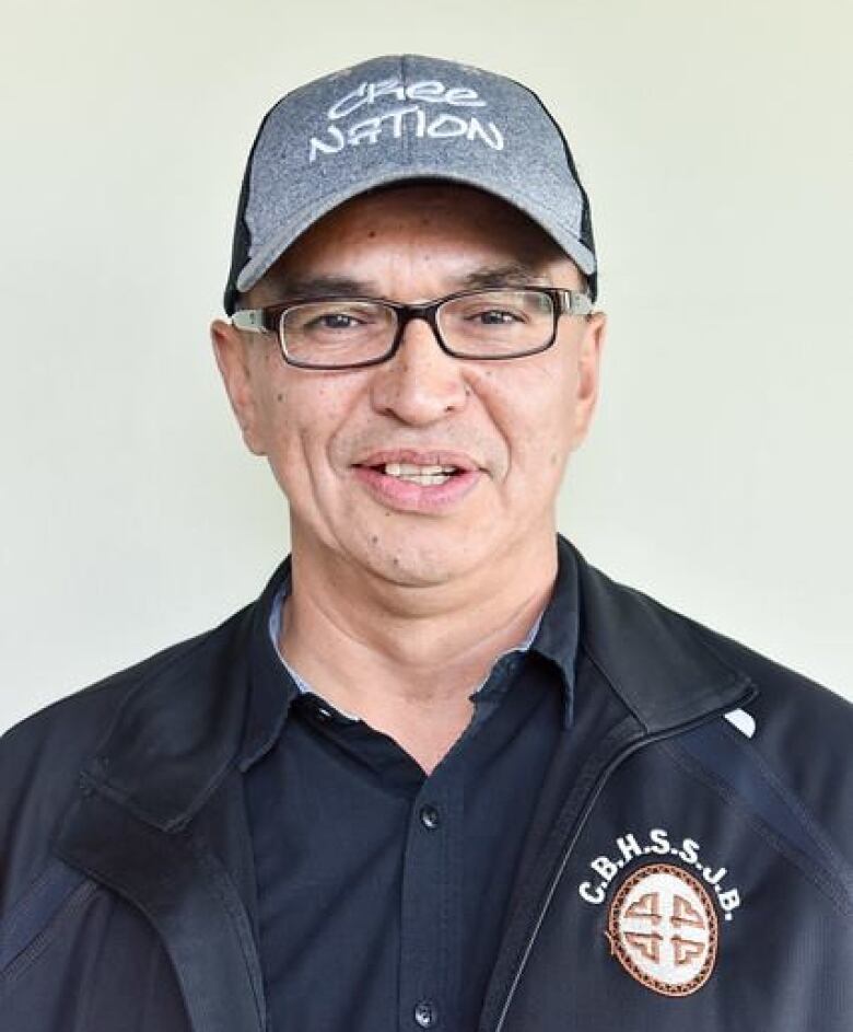 A cree man in a baseball hat looks at the camera.