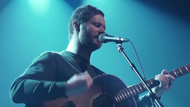 A man is pictured holding a guitar and singing into a mic.