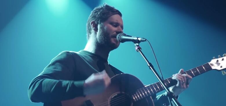 A man is pictured holding a guitar and singing into a mic.