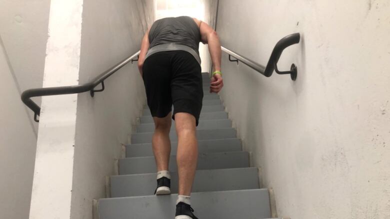 A man viewed from behind climbing a flight of concrete stairs. 