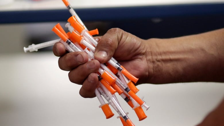 A hand holding a fistful of syringes and needles.