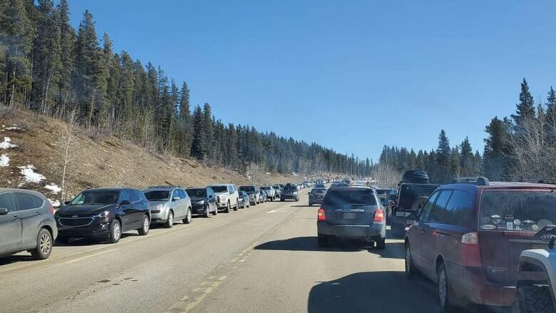 Cars parked bumper to bumper along the shoulders a narrow mountain highway.