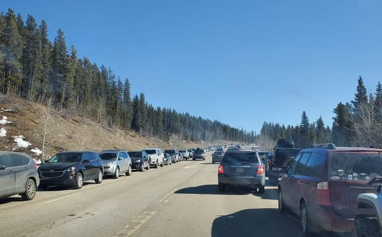 Cars parked bumper to bumper along the shoulders a narrow mountain highway.