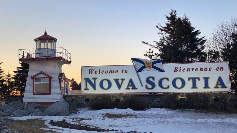 A sign reads Welcome to Nova Scotia in both English and French. There is snow on the ground and the sun is setting in the distance.