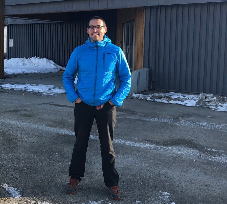 A man stands outside the Yukon convention centre in daylight. There is snow on the ground.