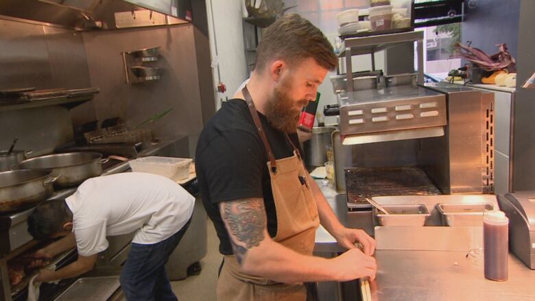 A man wearing an apron can be seen working in a restaurant kitchen. 