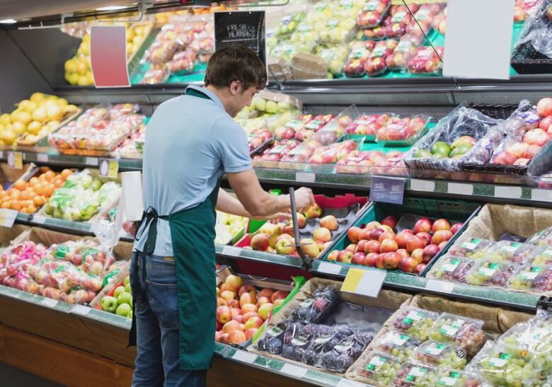 A man in an employee's apron sorts fruit in a grocery store aisle.