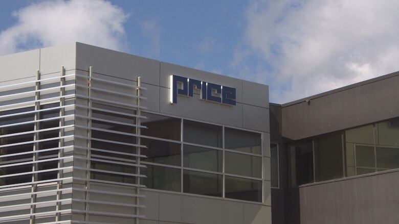 A grey building is seen with window panels and a sign with the name 