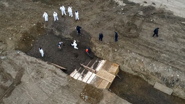 Workers wearing personal protective equipment work in a trench on Hart Island.