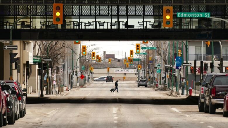 A lone person in the distance walks across an otherwise empty street in a city downtown.