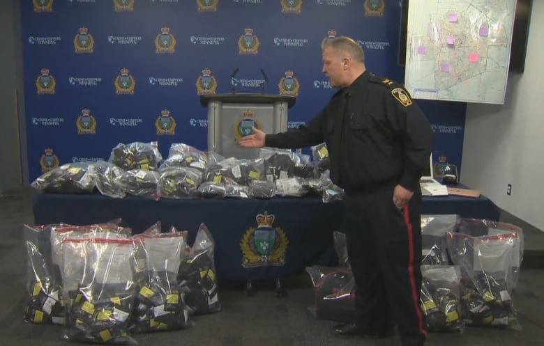 A man in a police uniform points at many bags of evidence