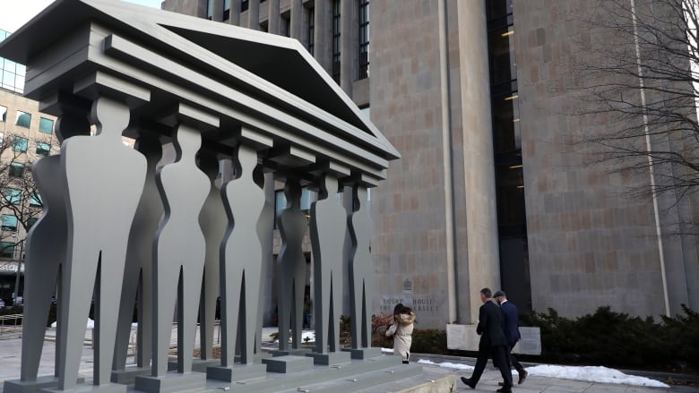 A sculpture of people making up columns under a roof sits outside a courthouse. 