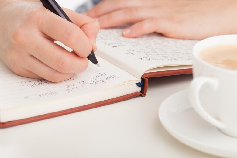 Hands writing in leather bound journal or diary with coffee.