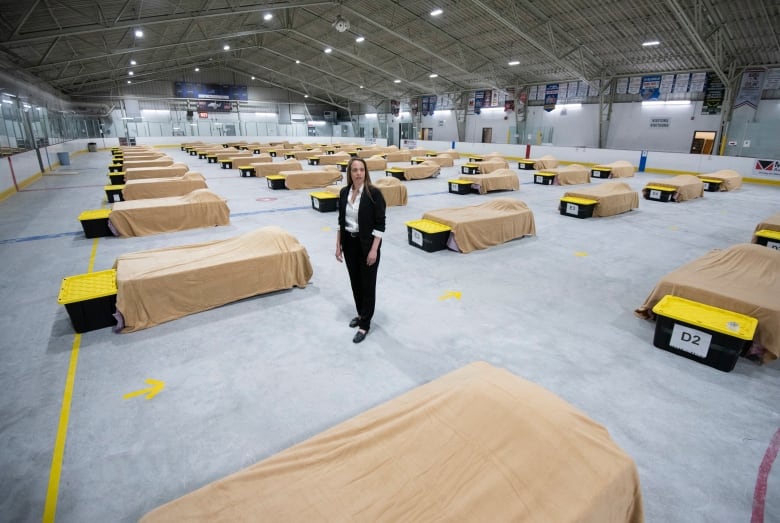 Someone stands on a rink pad with no ice. Instead, there are rows of beds with brown sheets.