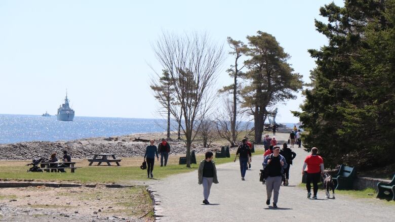 Pedestrians enjoy a sunny day by walking through Point Pleasant Park. The water can be seen in the background.