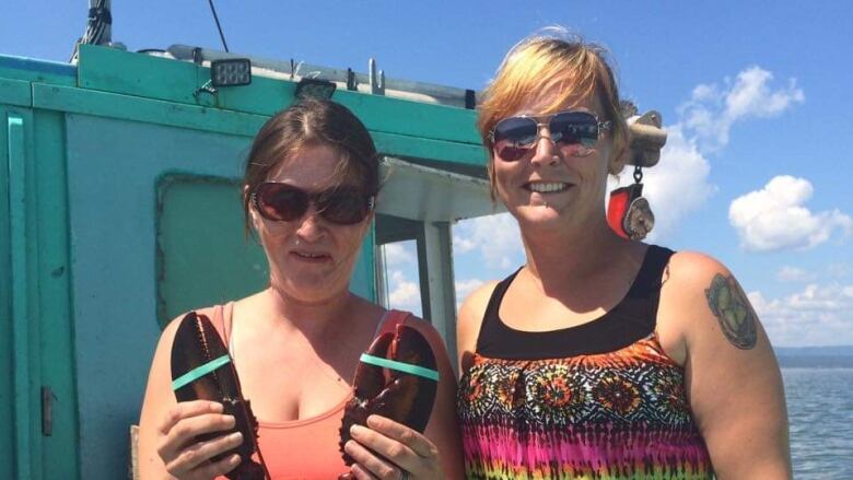 Two women on the deck of a boat with one holding a lobster.