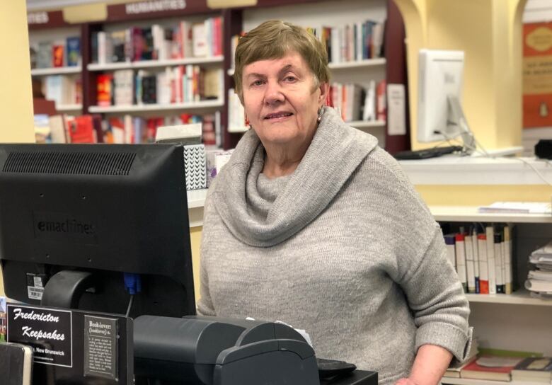 A woman standing behind a till with a bookshelf in the background