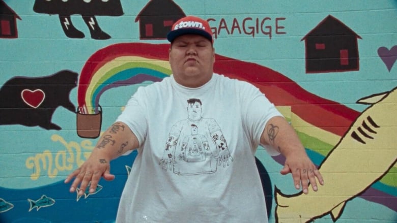 Musician Jesse Koenig stands in front of graffiti with his arms outstretched.