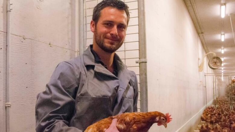 A man holds a hen inside a barn full of hens