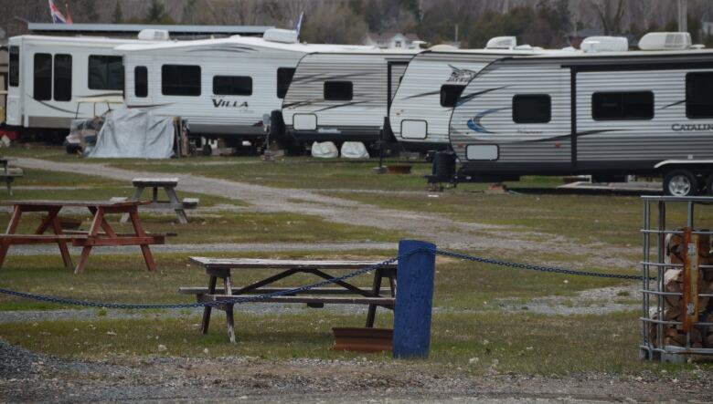 A row of trailers are parked closely together on a grassy flat field with picnic tables in the foreground. 