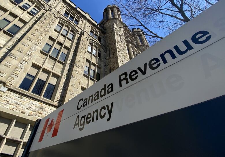 A sign reading 'Canada Revenue Agency' stands outside of a large stone building. 