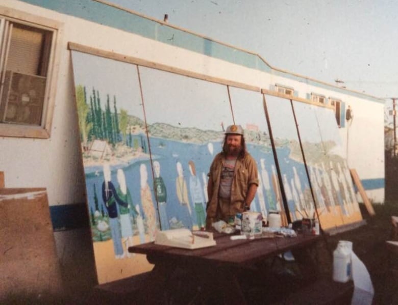 Young-ish man paints a large wooden mural