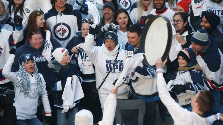 A crowd of hockey fans at a party celebrate while dressed in white and blue Winnipeg Jets clothing. 