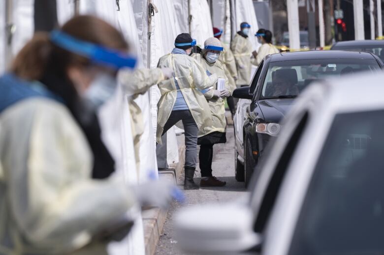 Health-care workers wearing masks and protective gowns meet people in their cars.