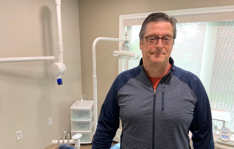 A man with glasses and a striped blue sweater standing in a dentist's office. 