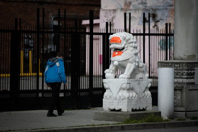 person in blue coat walks by lion statues covered in orange tape