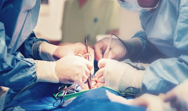 Two doctors dressed in blue scrubs lean over a patient while performing surgery.