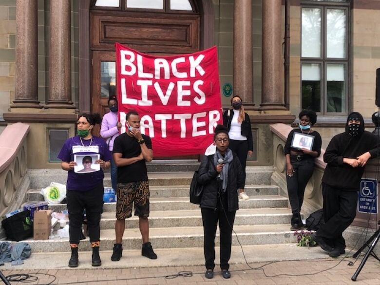 Some protesters stand in front of a large sign that reads 