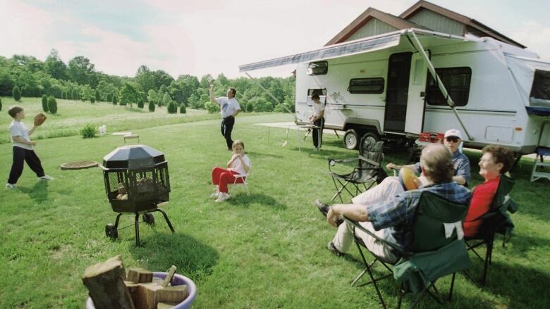 A trailer is set up on a grassy spot, with people of all ages enjoying themselves. 