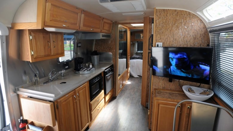 the inside of a trailer showing countertops, kitchen, a bedroom in the background and a TV showing the film Avatar. 