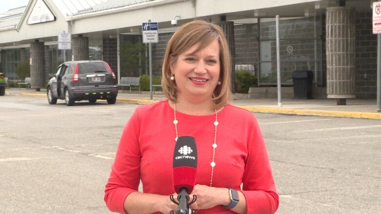 A woman wearing a red shirt stands outside an airport.