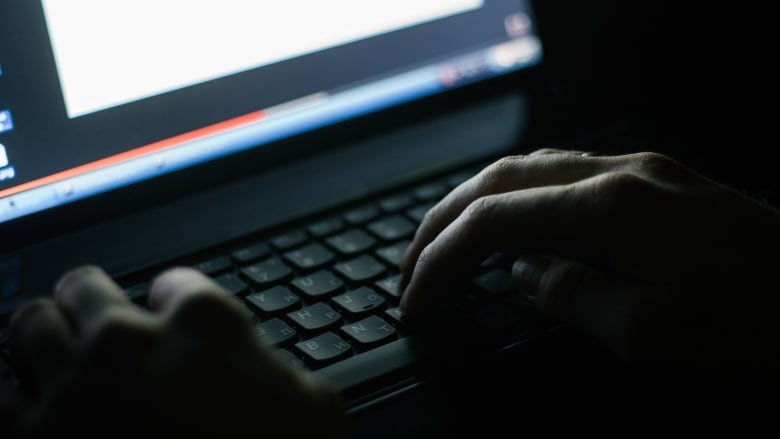 A closeup shows hands on a computer keyboard in a darkened room.