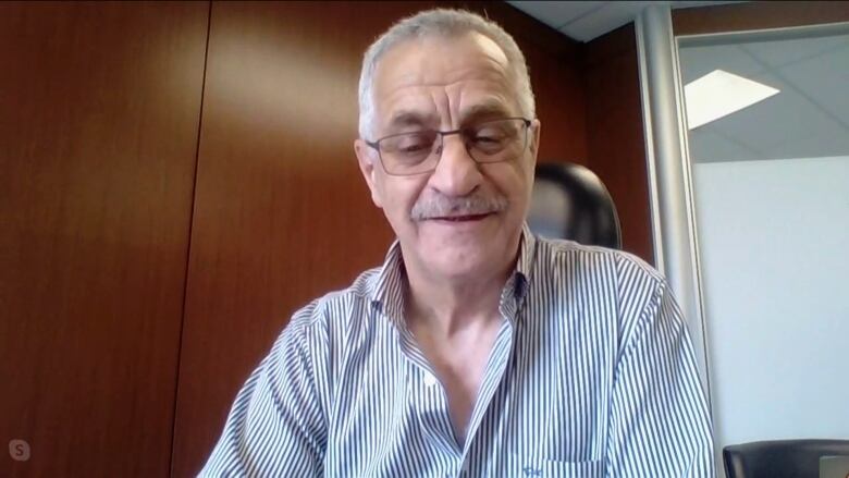 A man with greying hair and a mustache looks down as he faces a camera.